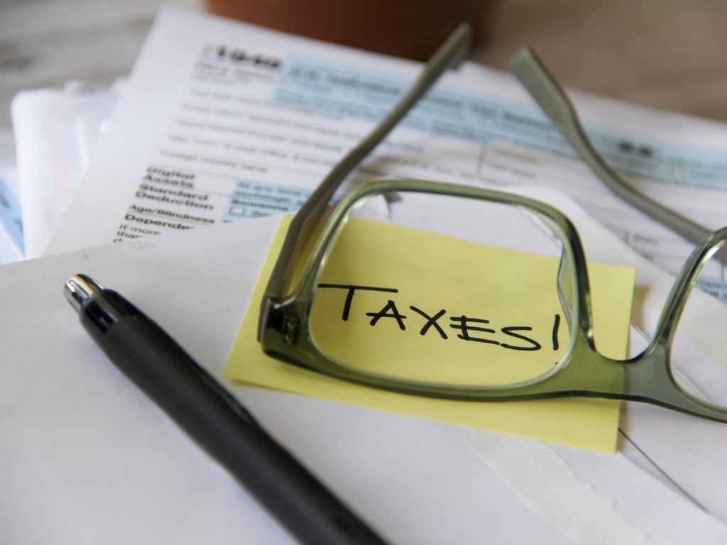 The word Taxes through the glasses of a person filing taxes with tax forms in background